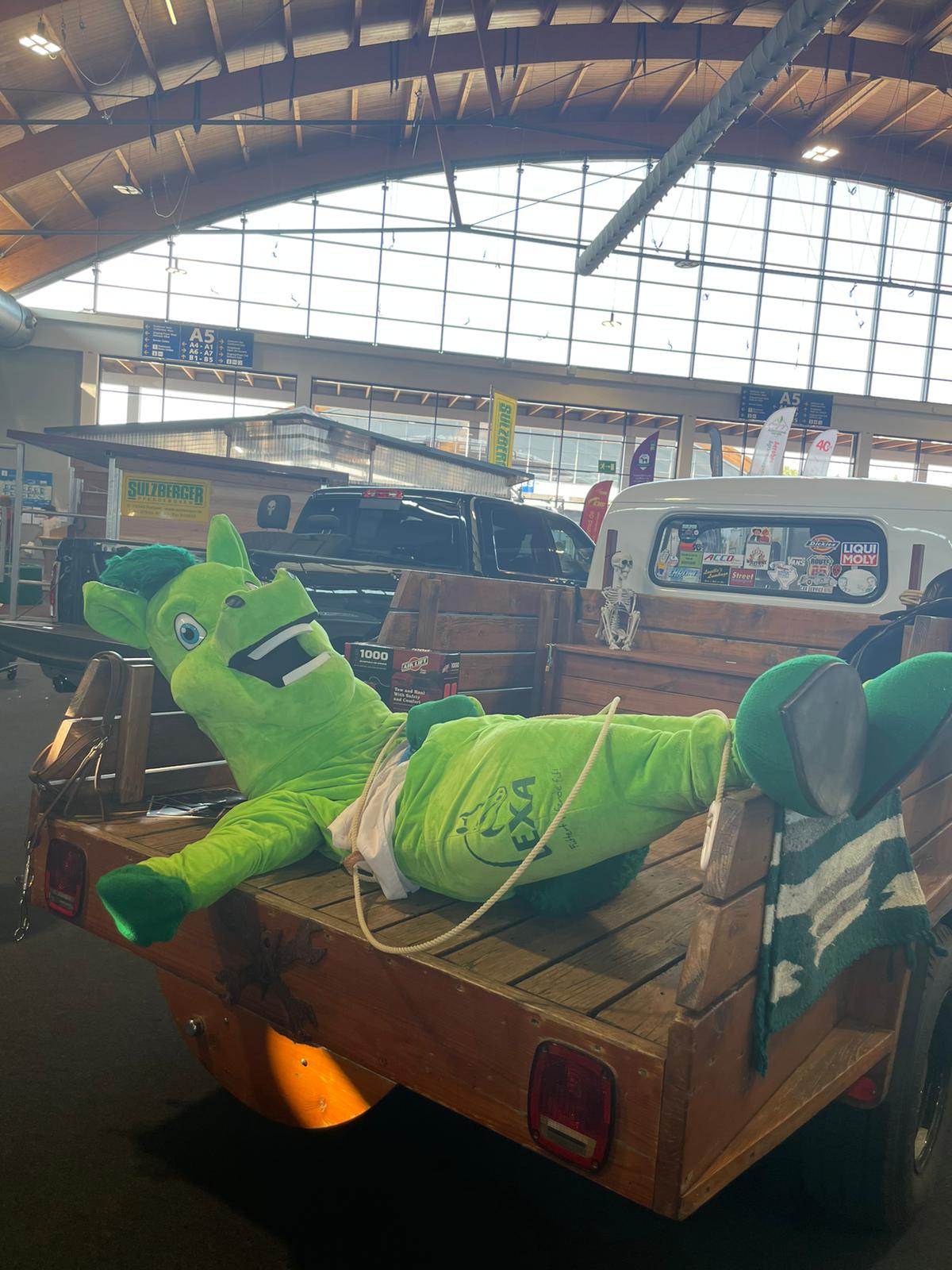 Grünes Maskottchen im Anhänger Ein grünes Maskottchen in einem Holzanhänger, lächelnd und entspannt.